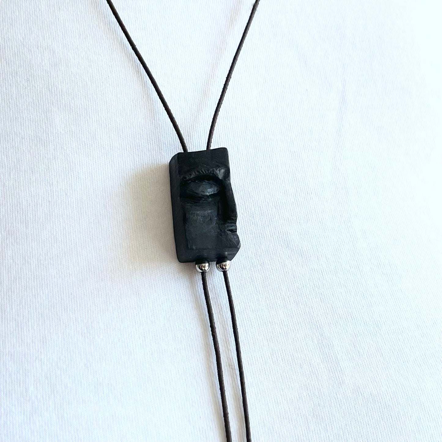 Close-up of bog oak pendant featuring a serene carved face, accented with stainless steel and black beads