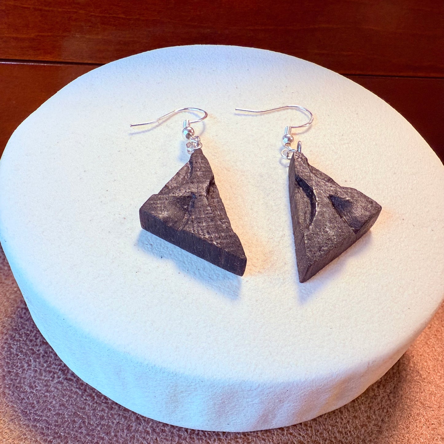 Handmade triangle earrings made from ancient Irish bog oak with surgical steel hooks, displayed on a natural background.