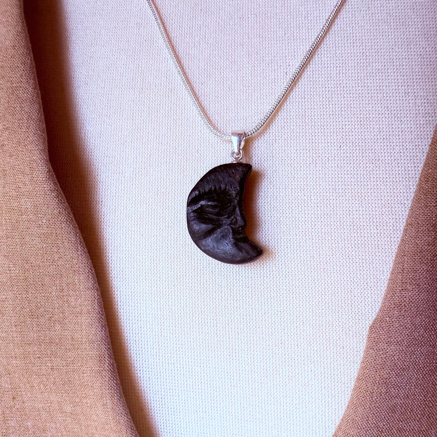Bog oak moon charm necklace displayed on natural linen background