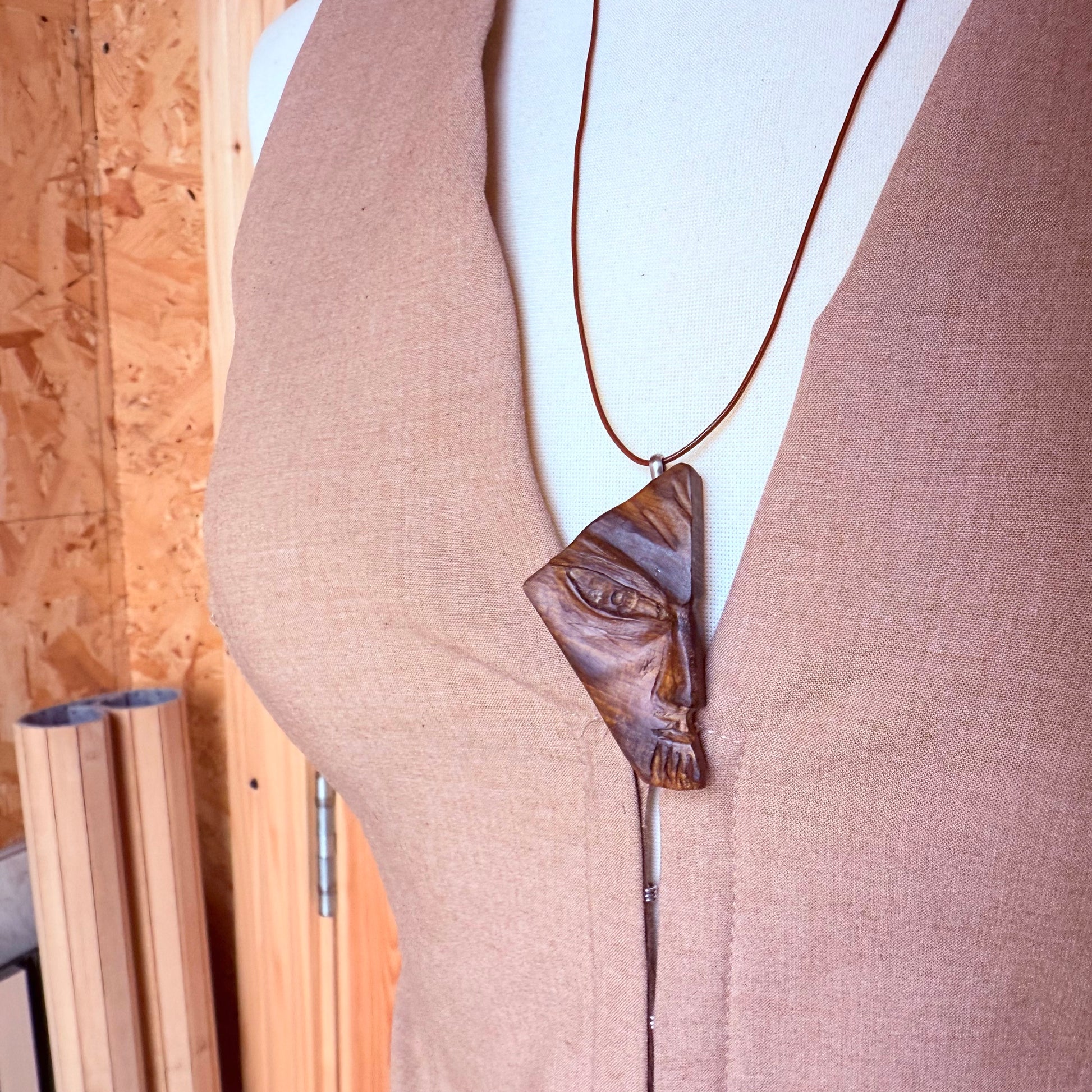 Mannequin wearing a necklace with a face-shaped pendant against a wooden background