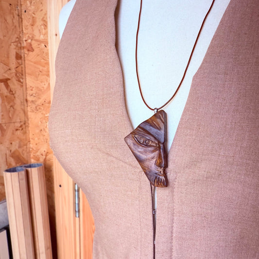 Mannequin wearing a necklace with a face-shaped pendant against a wooden background