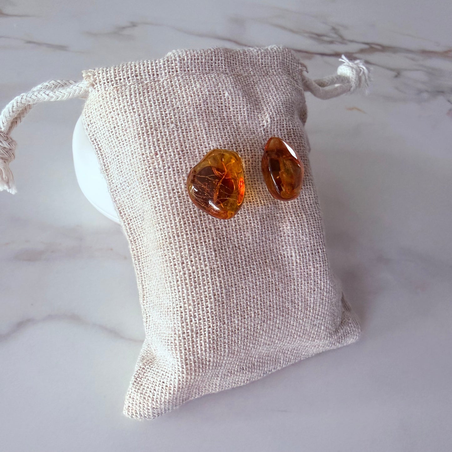 Amber-colored earrings on a textured fabric pouch against a marble background