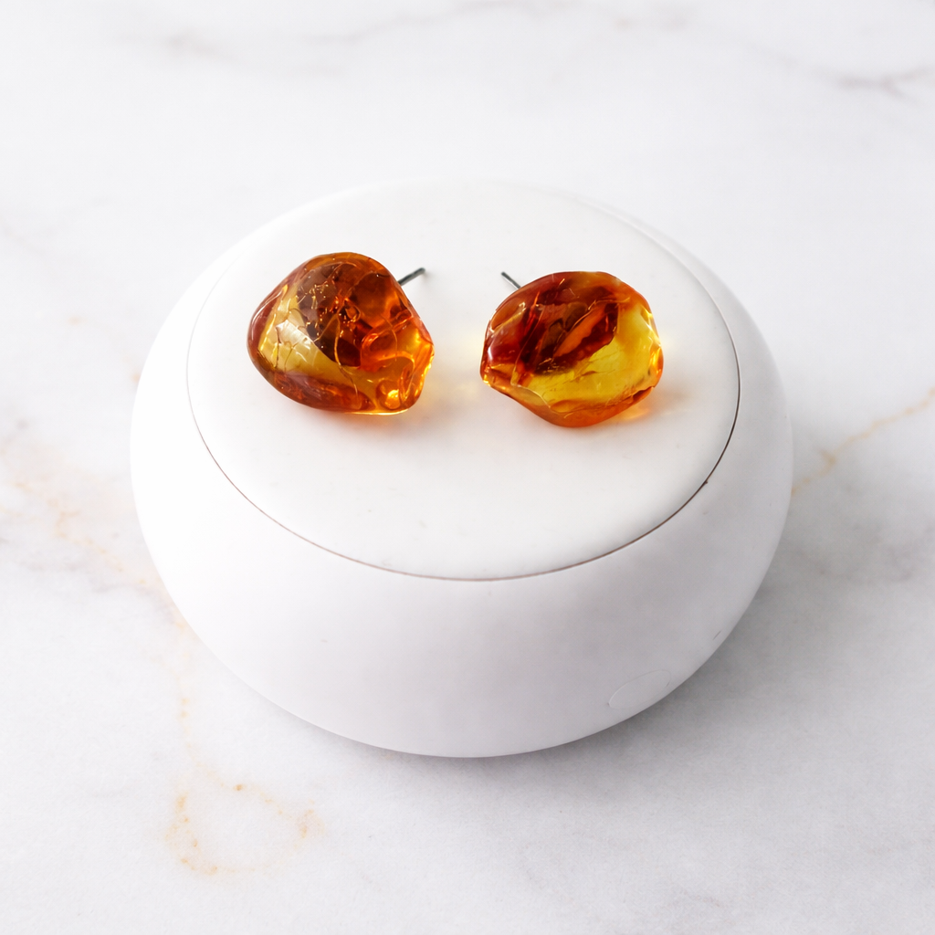 Amber heart-shaped earrings on a white round stand with a marble background