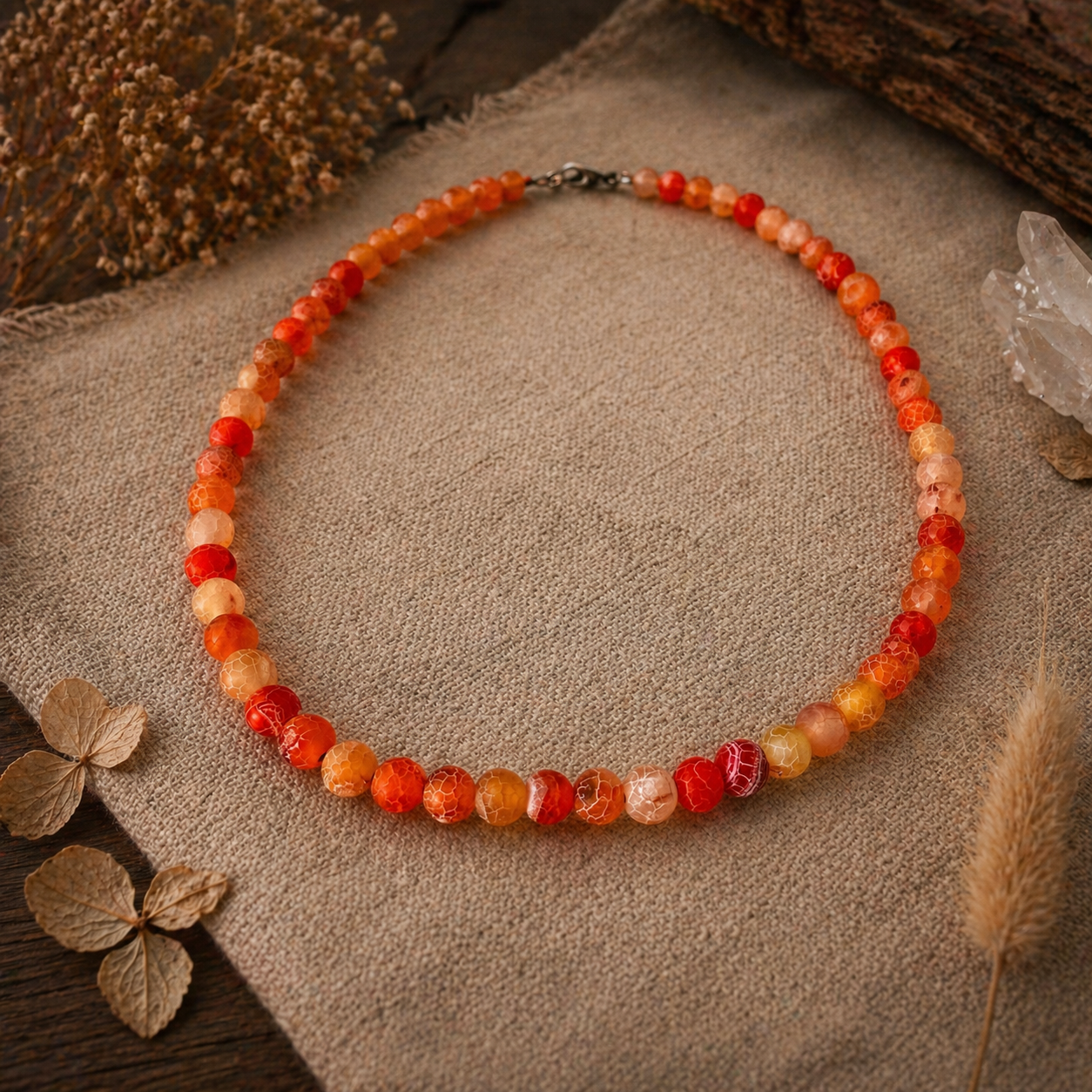 Necklace with red and orange beads on a textured surface with dried leaves and crystals.
