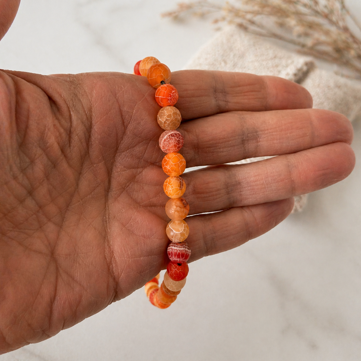 Hand holding a beaded bracelet with orange and red beads on a neutral background