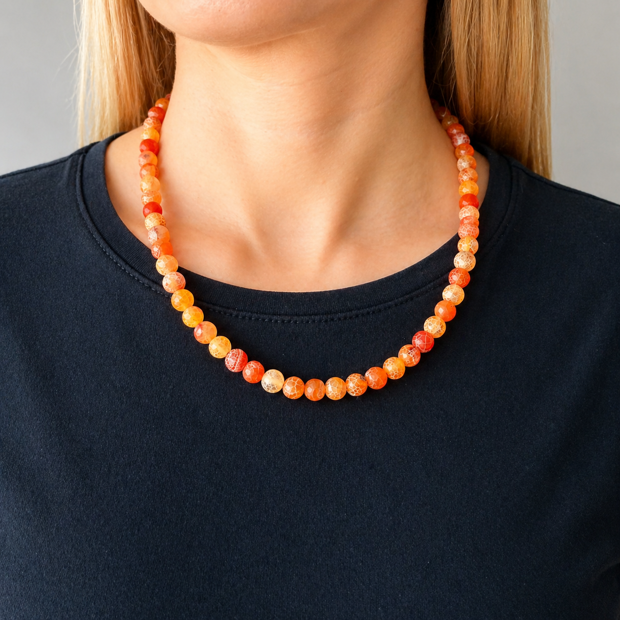 Necklace with orange beads worn by a person against a neutral background