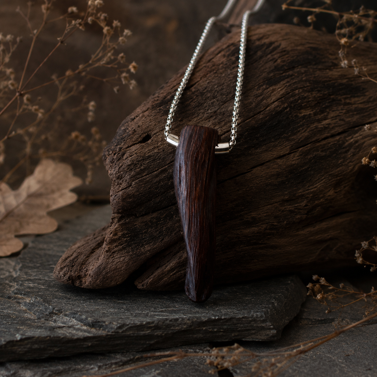 Wooden pendant necklace on a dark stone surface with dried leaves