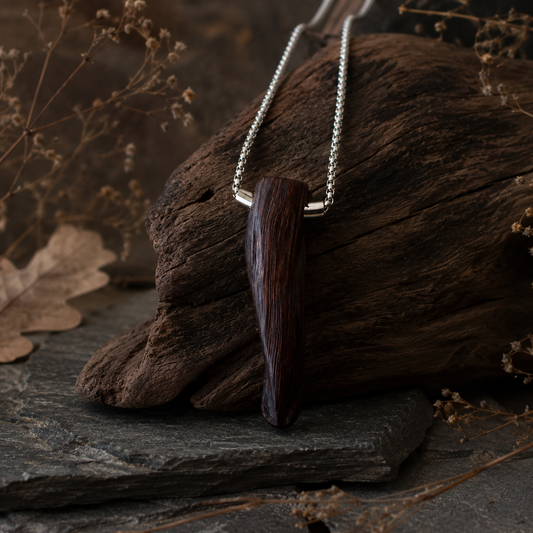 Wooden pendant necklace on a dark stone surface with dried leaves