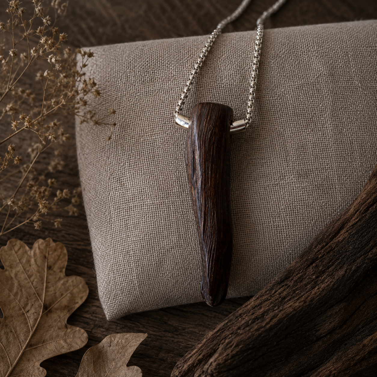 Wooden pendant necklace on a textured surface with dried leaves and branches.
