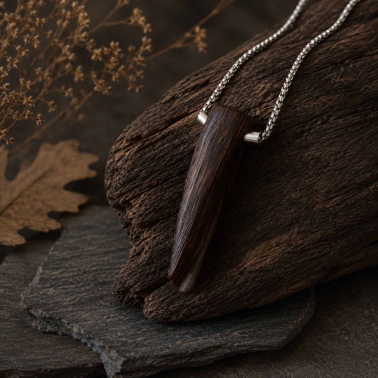 Wooden pendant necklace on a dark stone surface with dried leaves