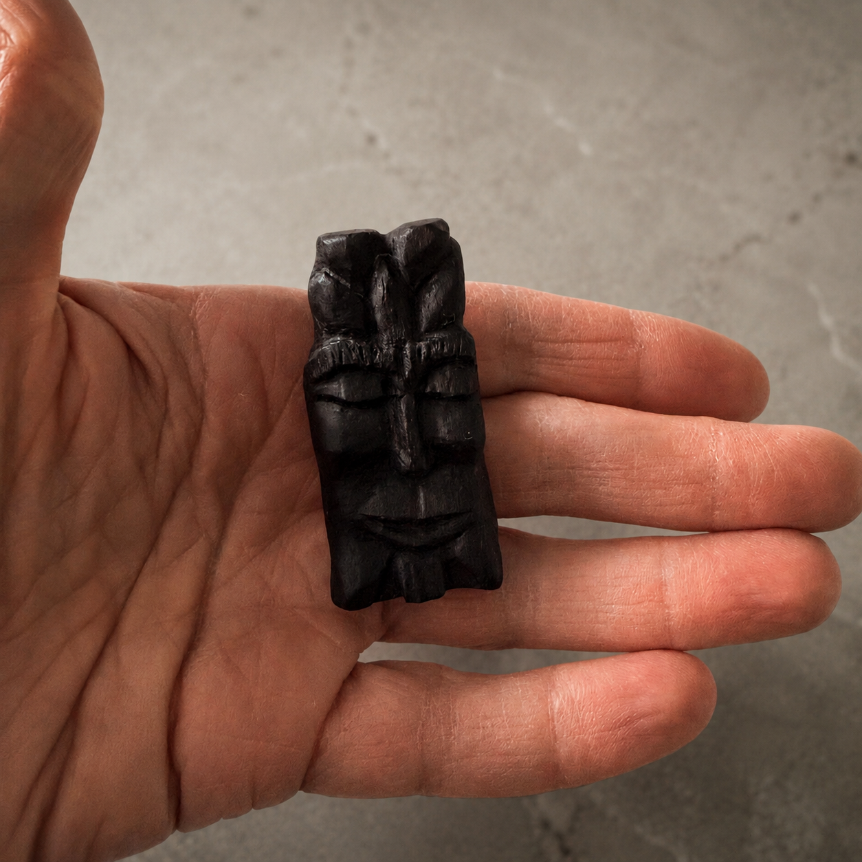 Hand holding a black stone carving against a neutral background