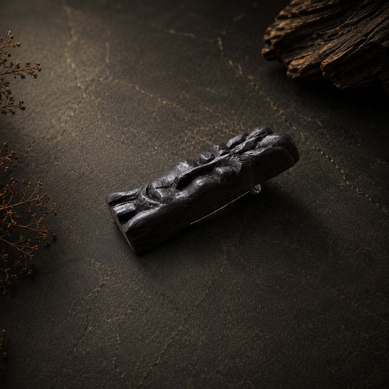 Black stone sculpture on a dark textured surface with dried plants.