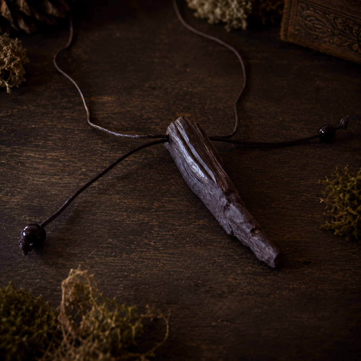 Wooden pendant necklace on a dark wooden surface with moss