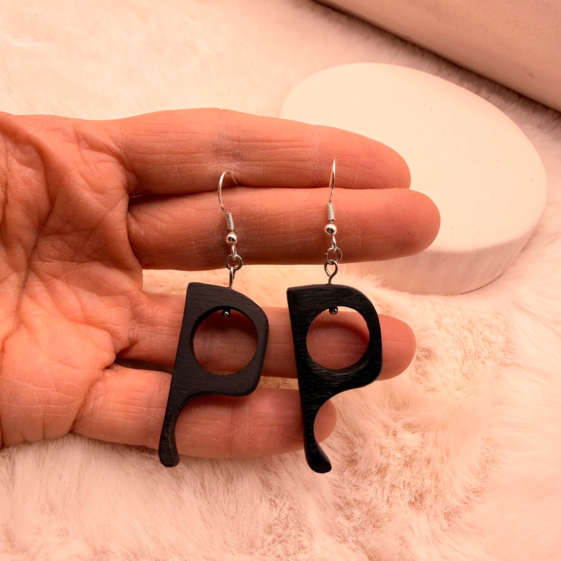 Black earrings held in a hand against a neutral background