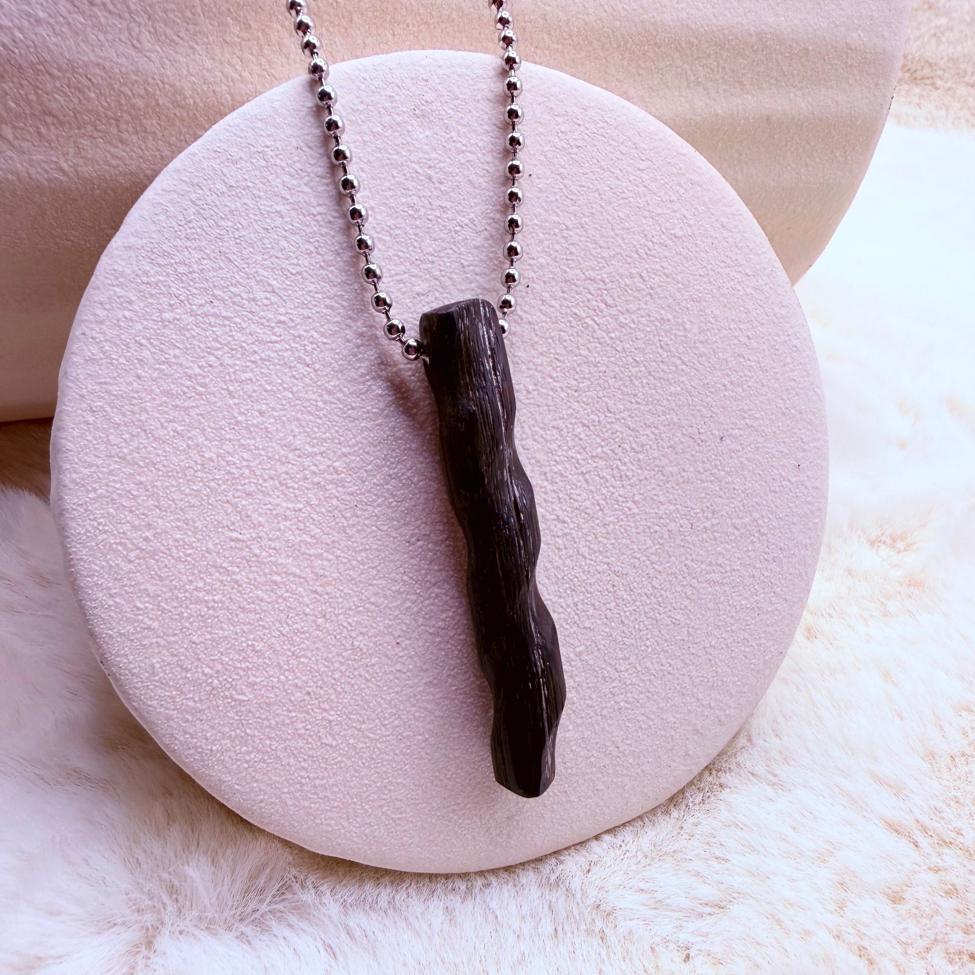 Necklace with a dark wooden pendant on a white stone surface