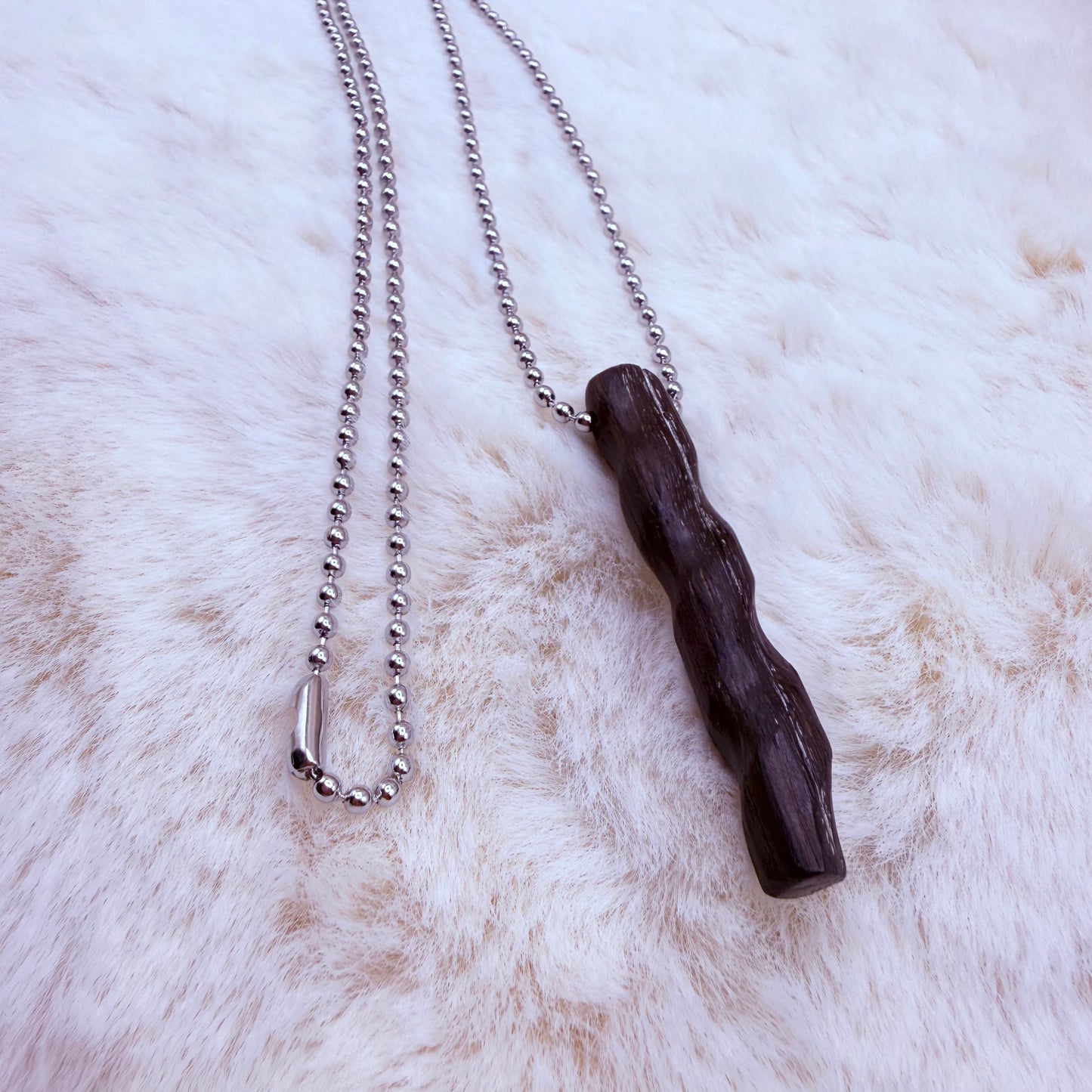 Necklace with a dark wooden pendant on a white fur background