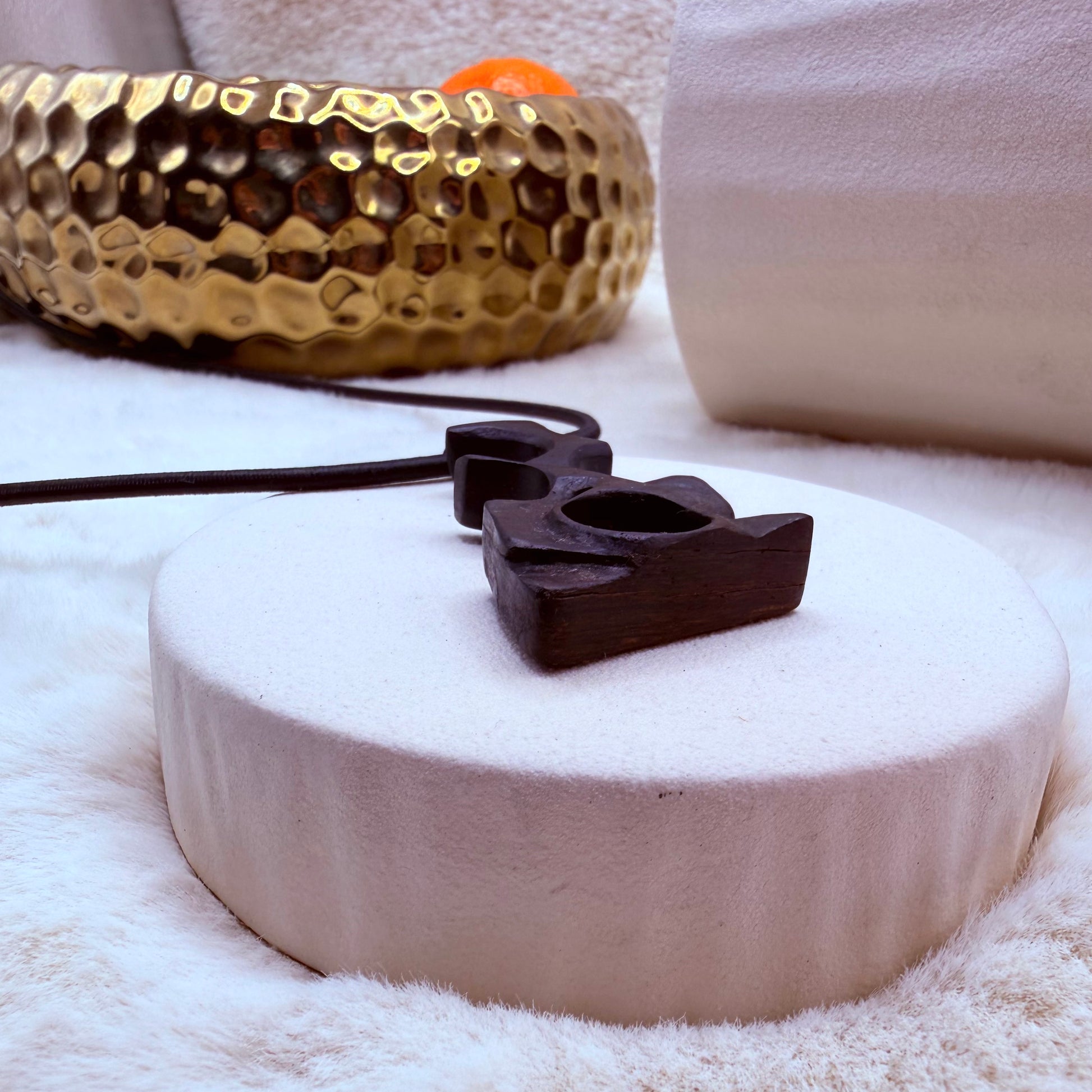 Black pendant on a white stone surface with a gold decorative item in the background