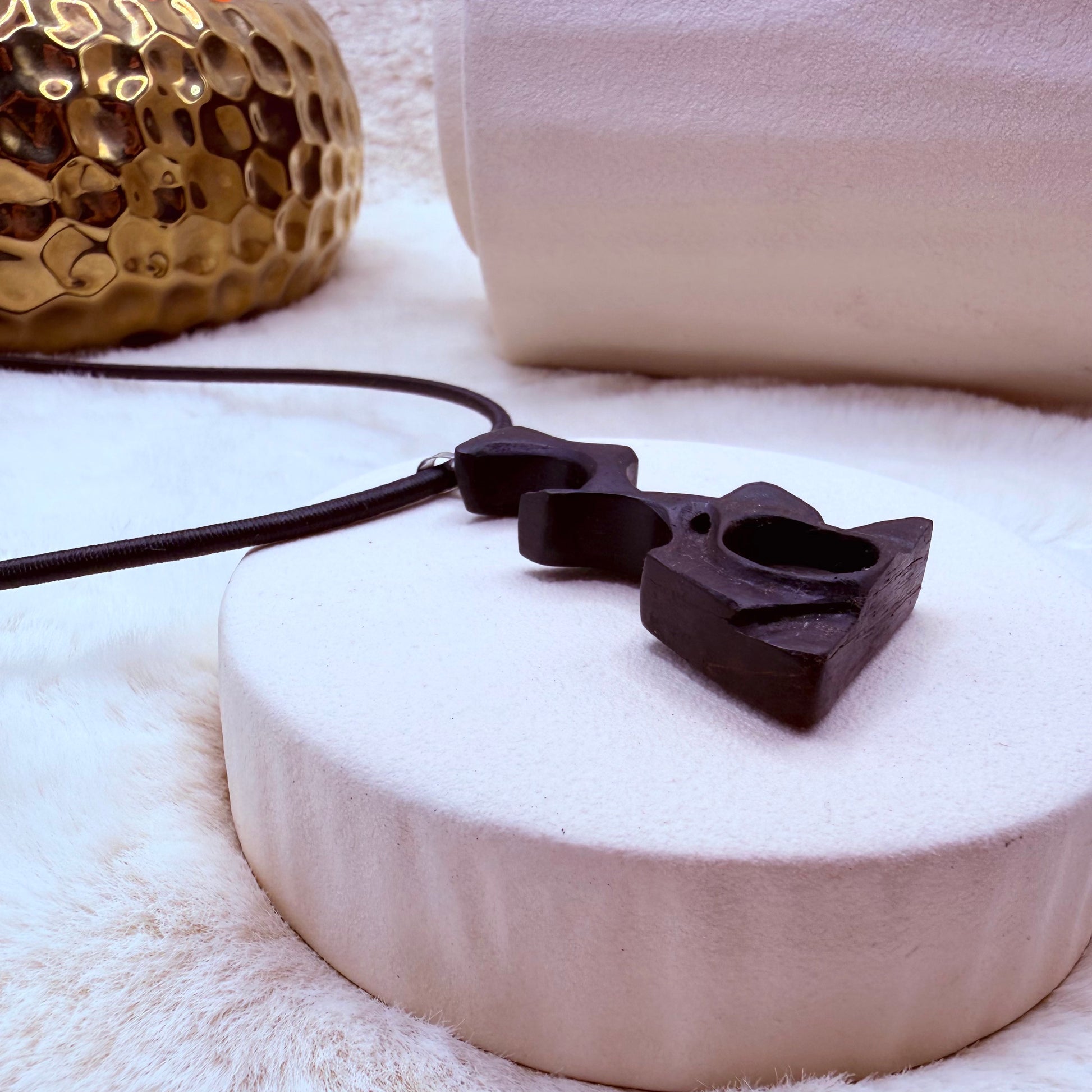 Black cat-shaped pendant on a white surface with a gold decorative object in the background