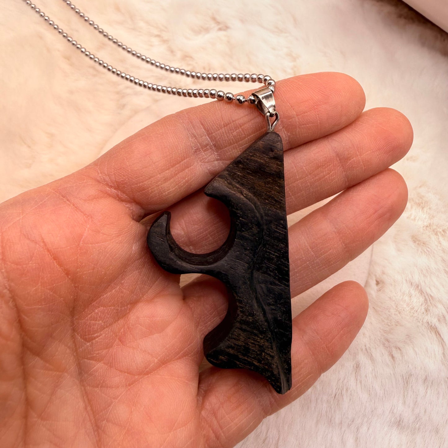 Hand holding a dark wooden pendant with a silver chain against a light background