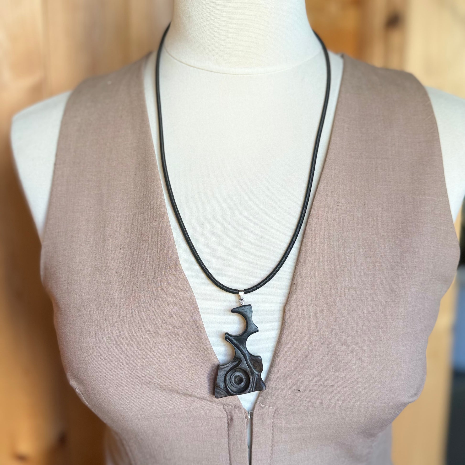 Hand carved black wooden pendant necklace on 3mm black rubber cord, three quarter view on white background