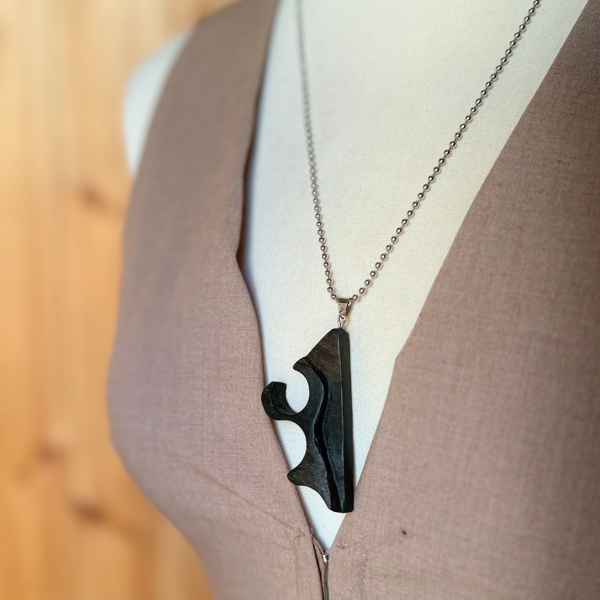 Black pendant on a chain worn by a person against a neutral background