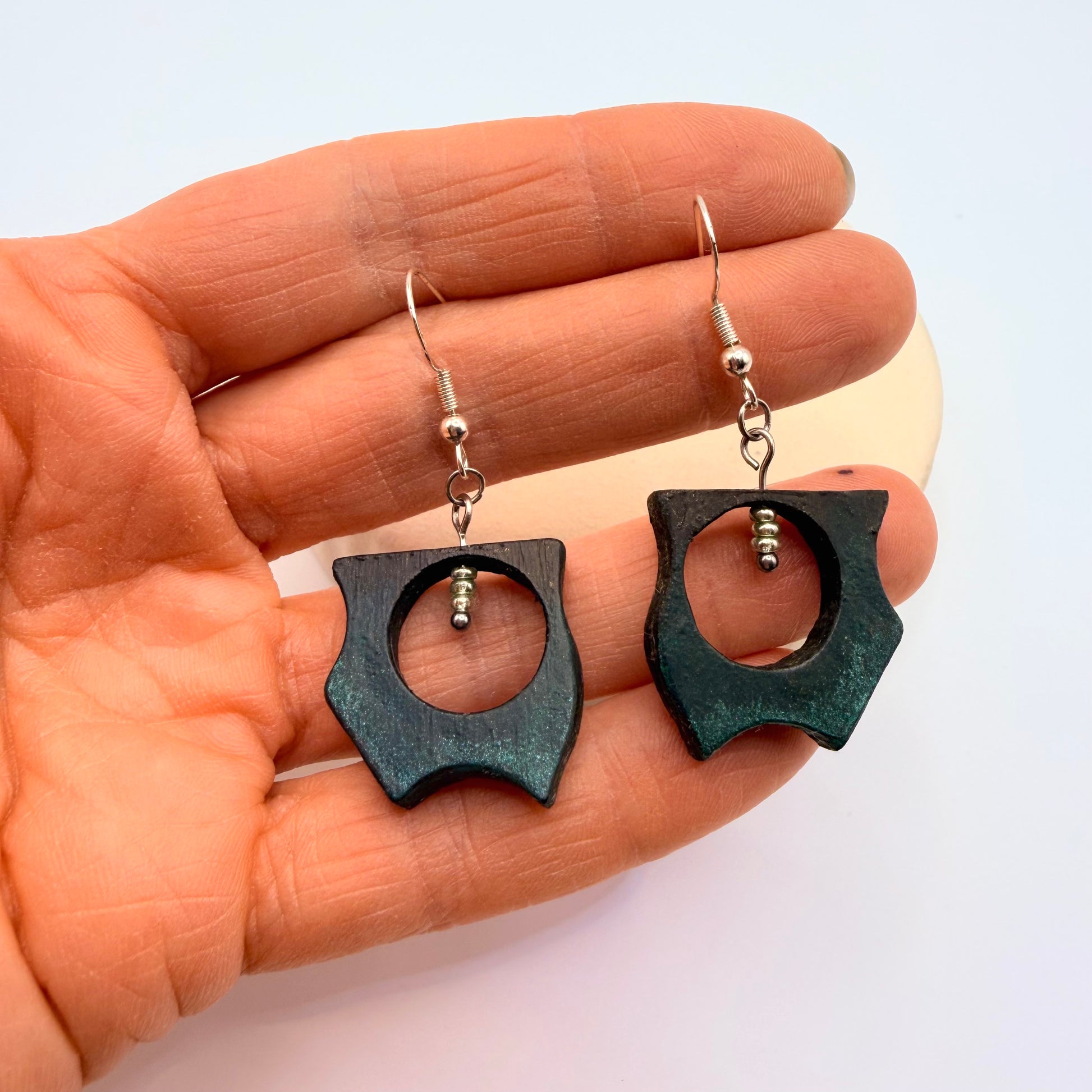 Black earrings held in a hand against a light background