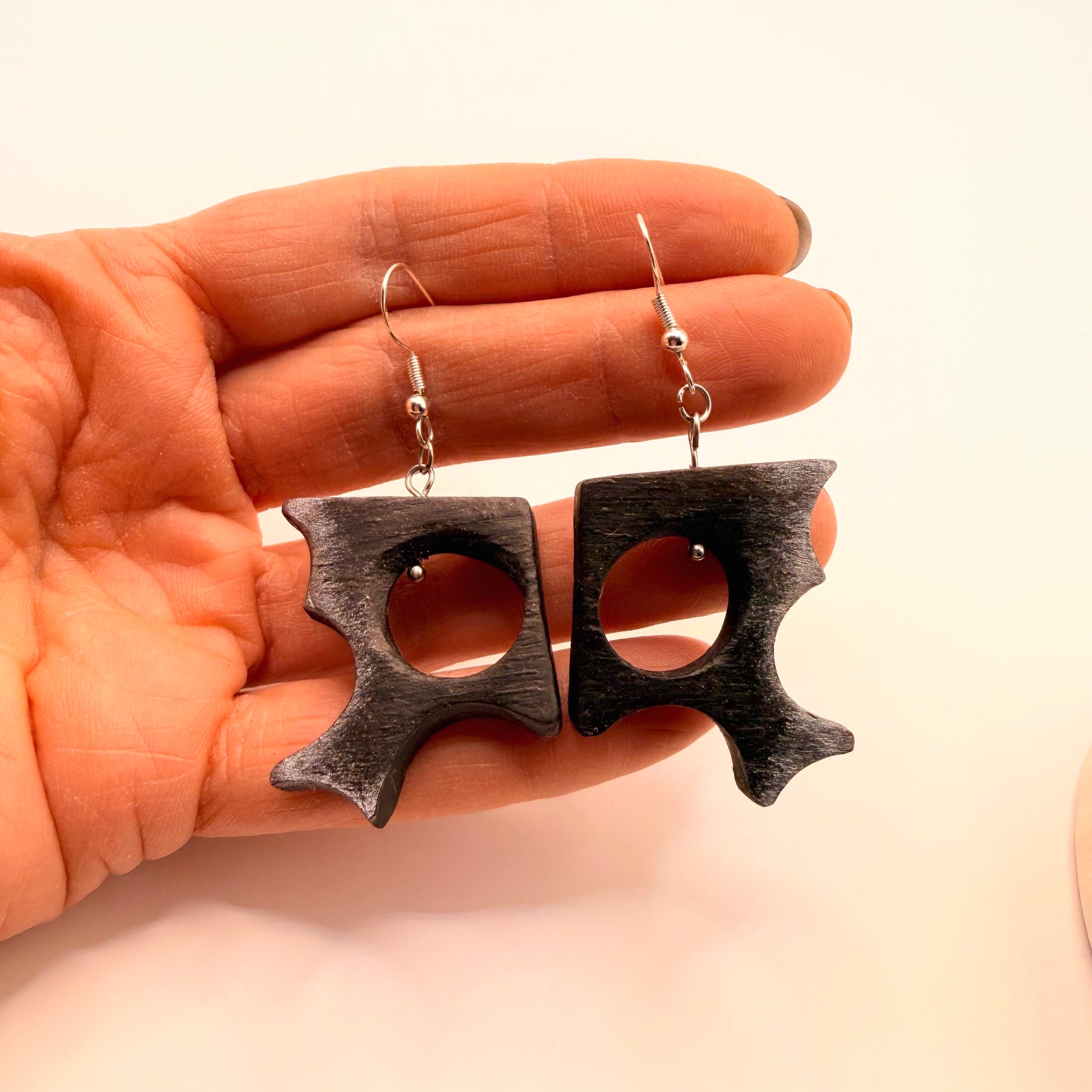 Wooden earrings held in a hand against a beige background