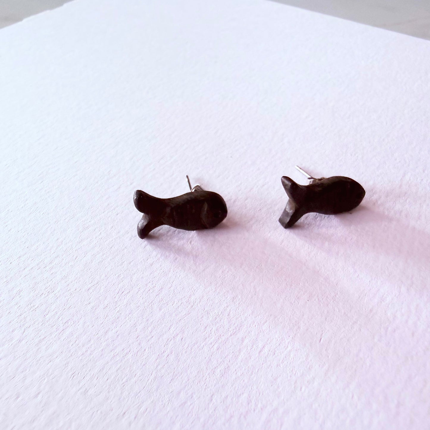 Black fish-shaped earrings on a white textured surface