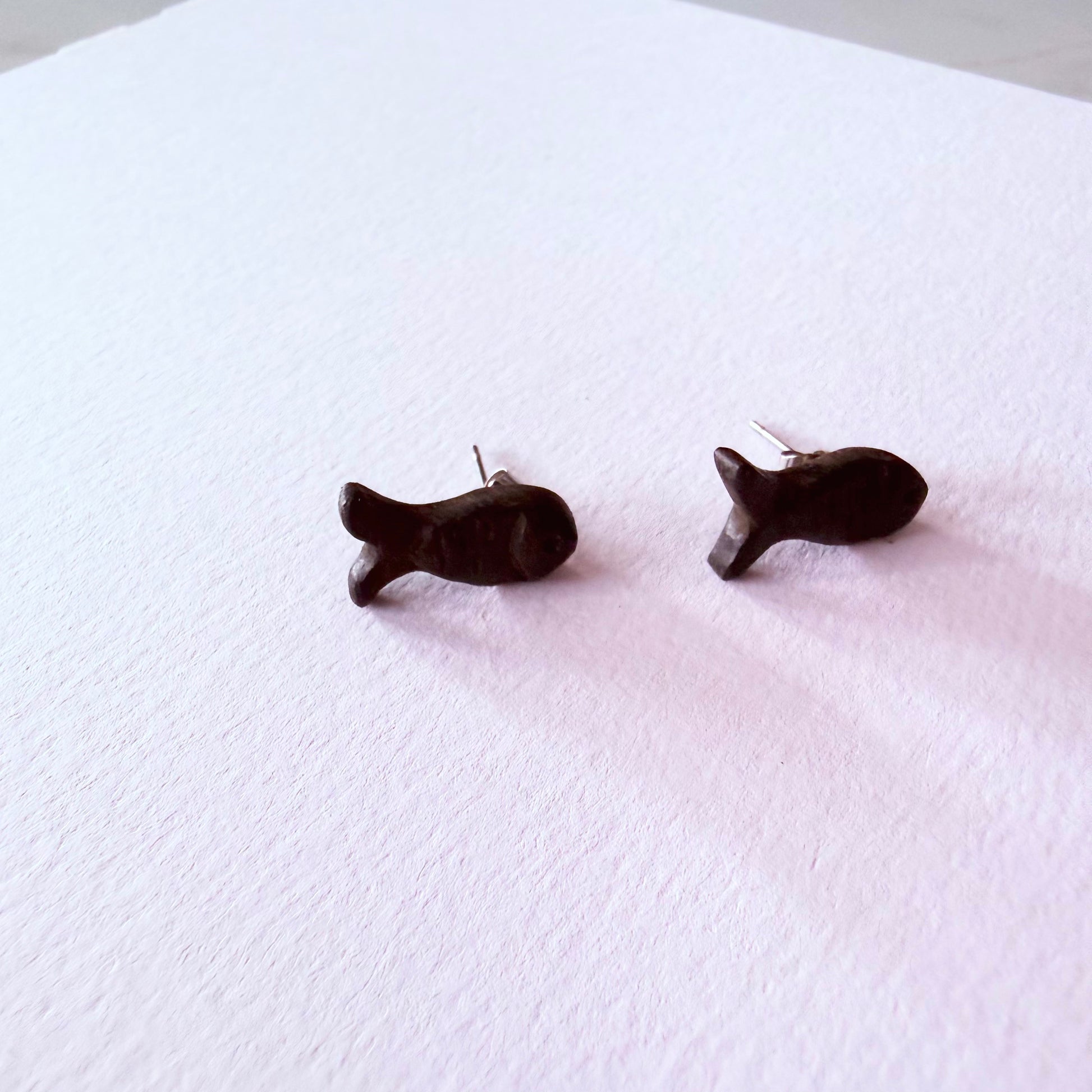 Black fish-shaped earrings on a white textured surface