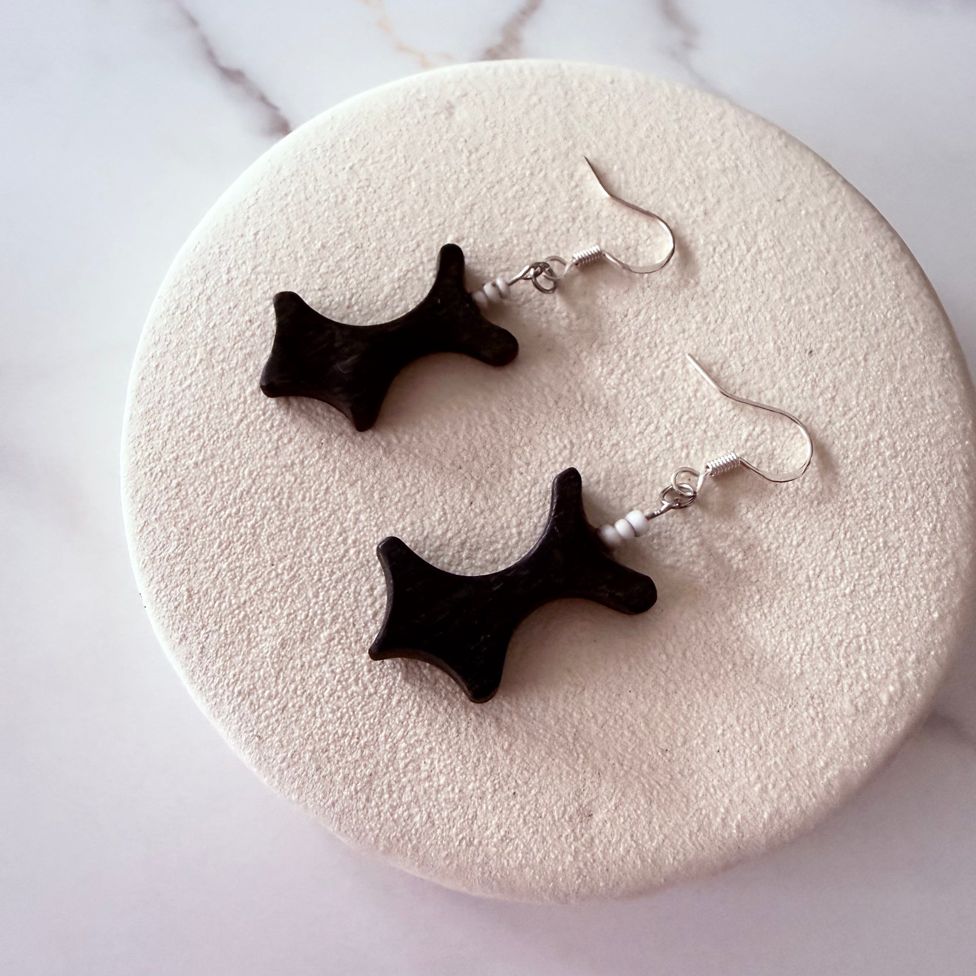 Black star-shaped earrings on a textured white surface