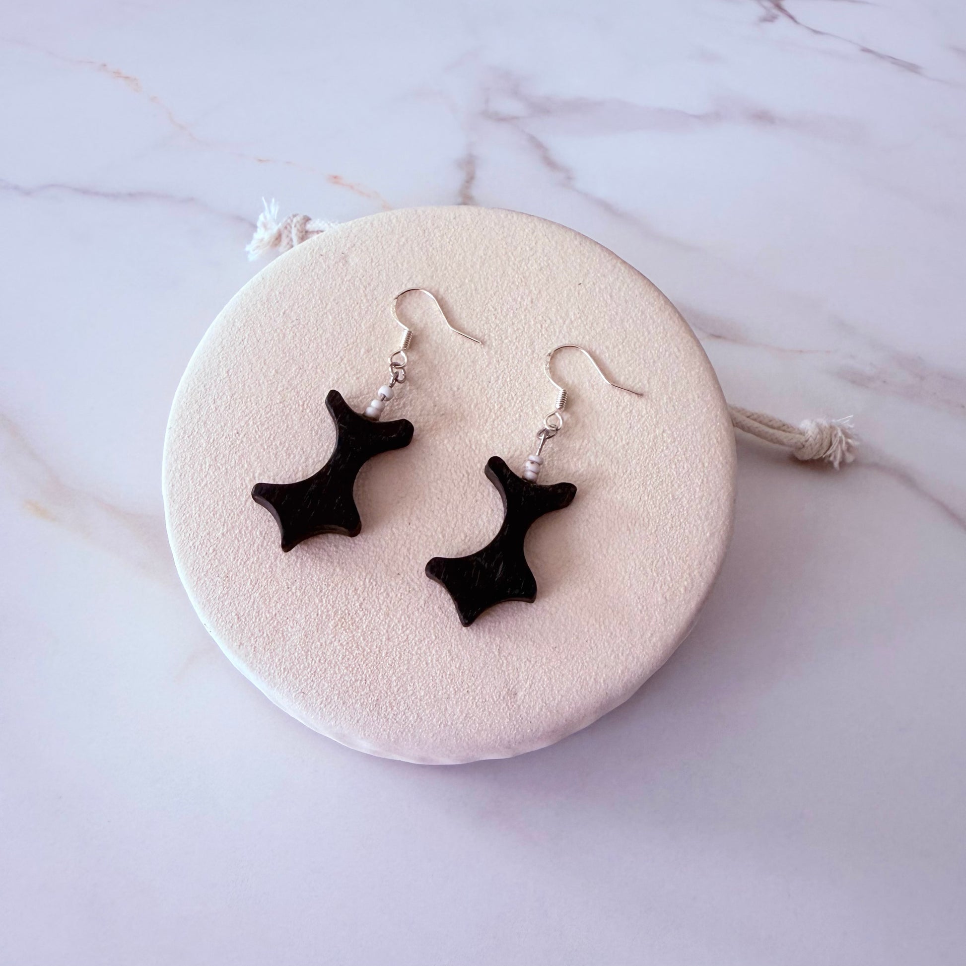 Black star-shaped earrings on a round white stone with a marble background