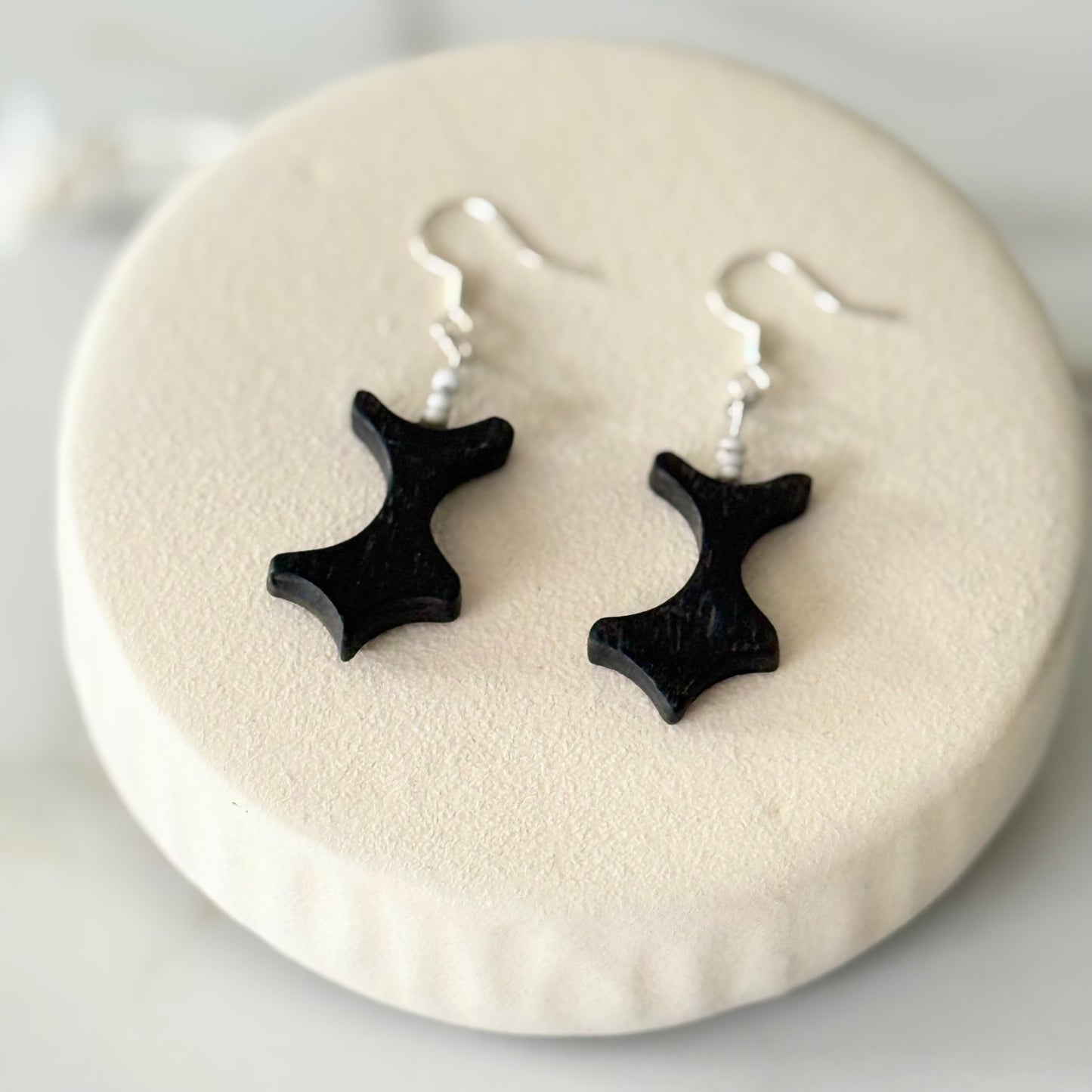 Black star-shaped earrings on a white circular stand.