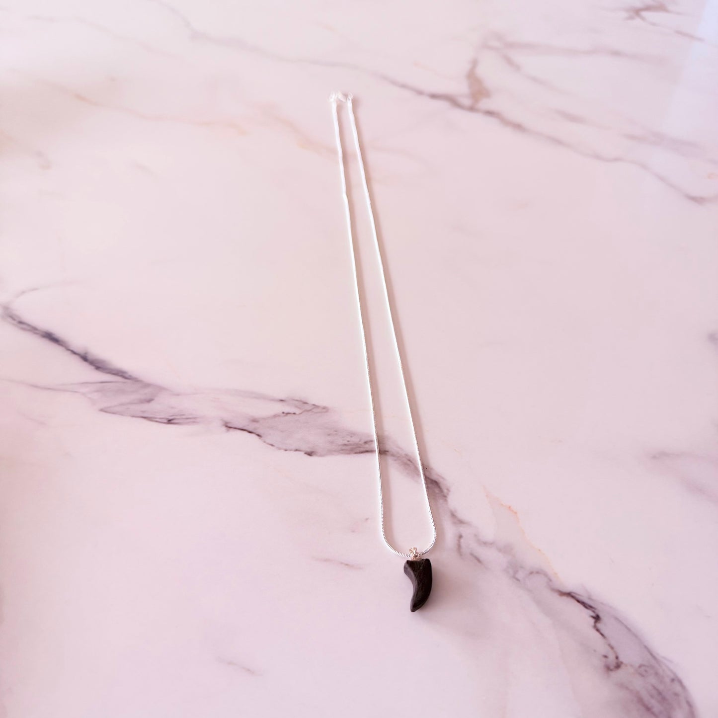 Silver necklace with a black pendant on a marble surface
