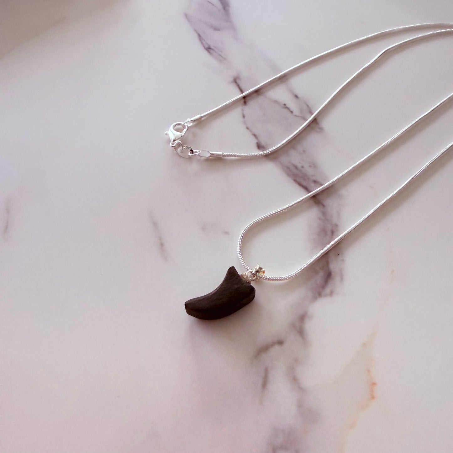 Necklace with a dark pendant on a marble surface