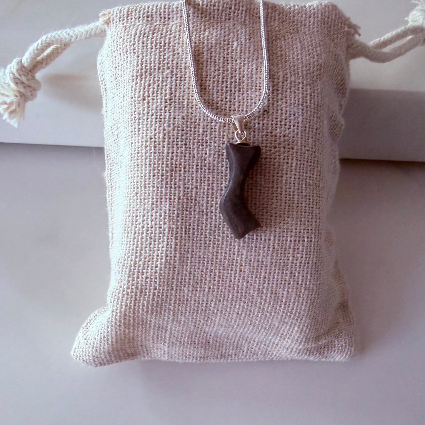 Necklace with a pendant on a textured fabric pouch against a white background