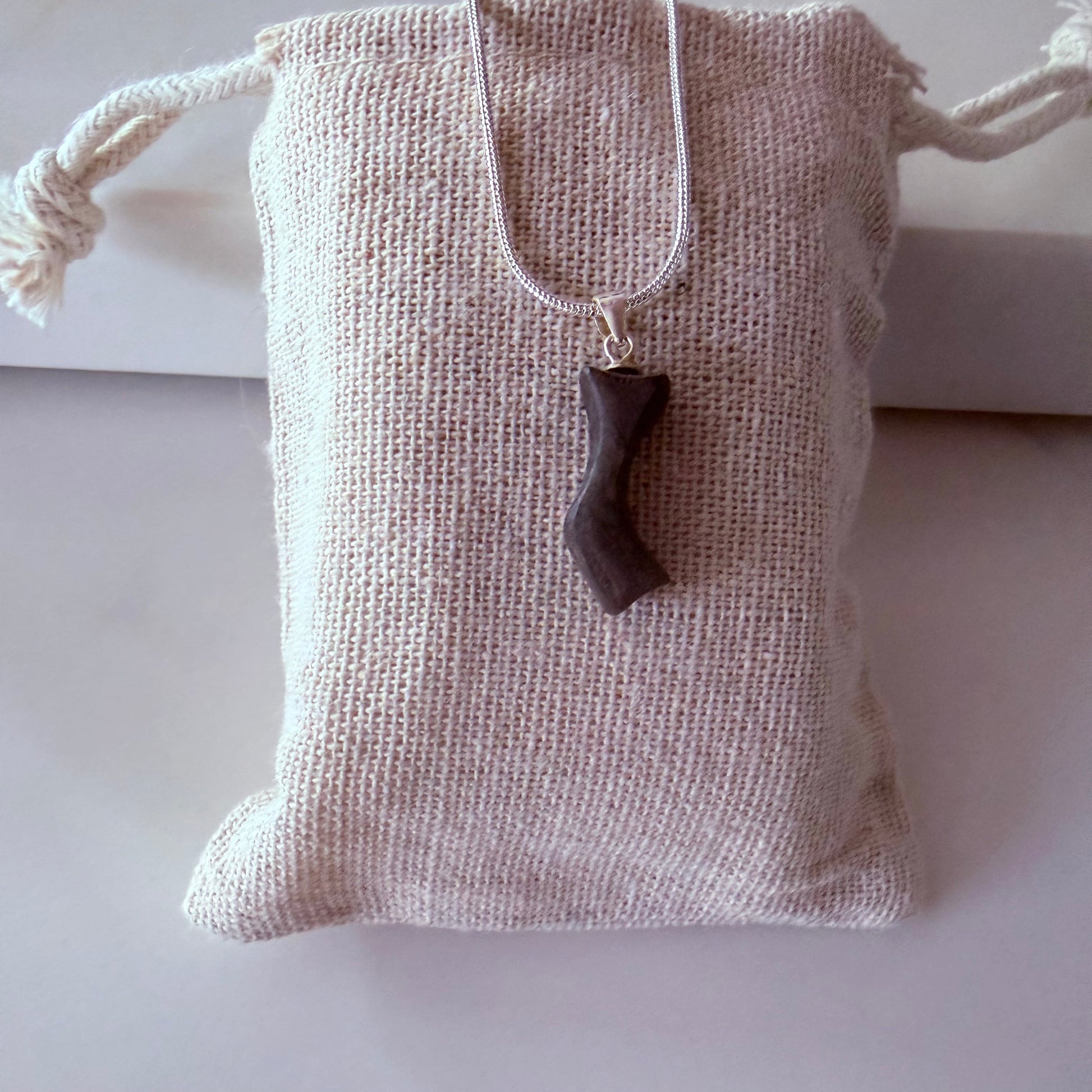 Necklace with a pendant on a textured fabric pouch against a white background