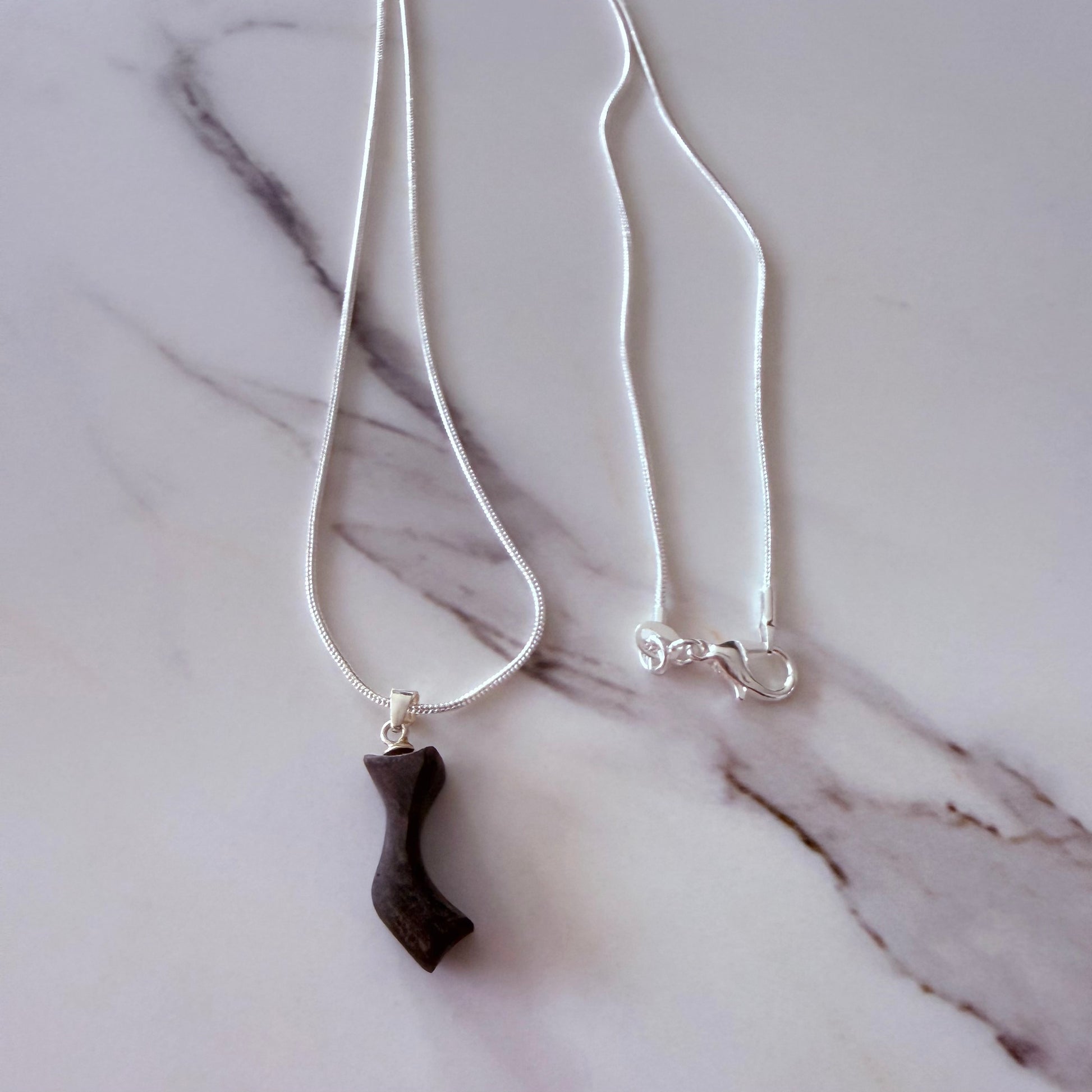 Necklace with a dark pendant on a marble surface