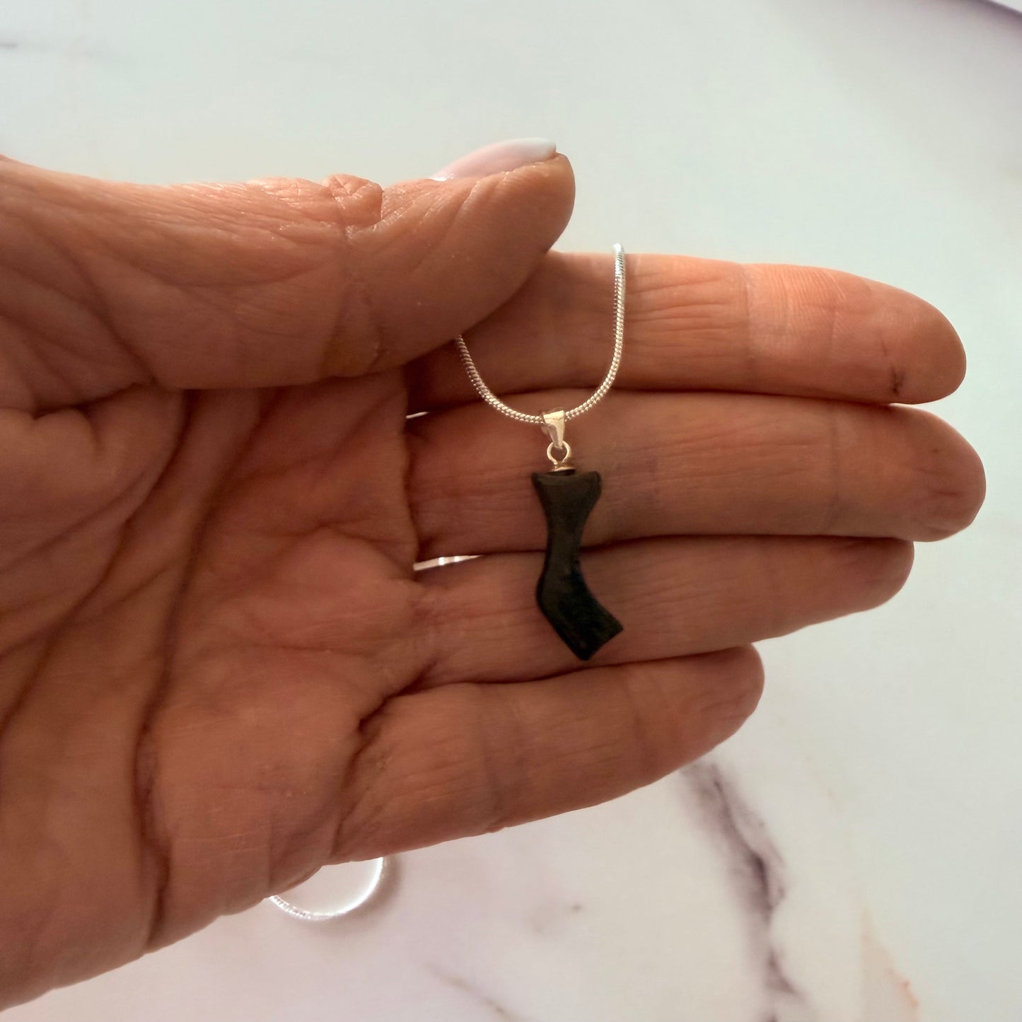 Hand holding a necklace with a black pendant on a light background