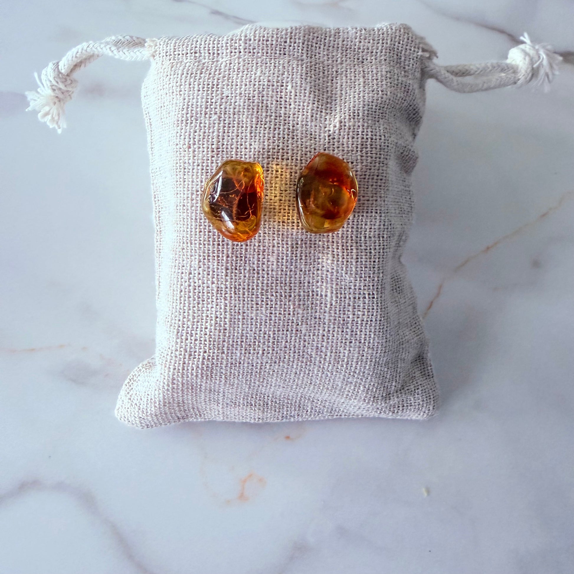 Pair of amber-colored bow-shaped earrings on a textured gray pouch against a marble background