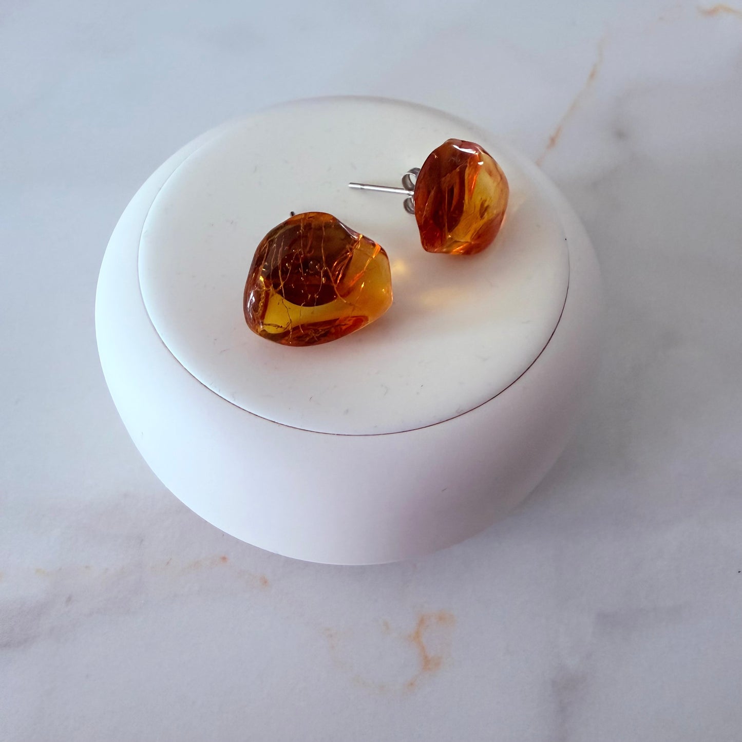 Amber-colored earrings on a white round stand with a marble background