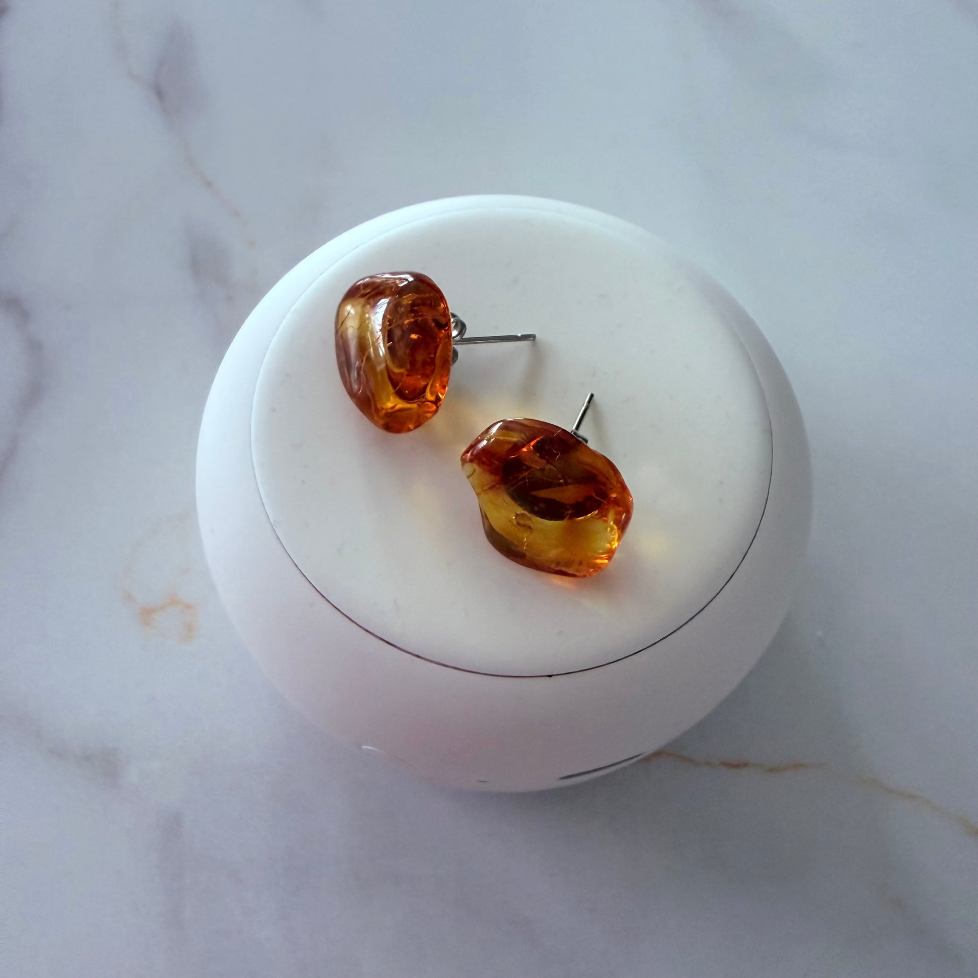 Amber-colored earrings on a white jewelry dish with a marble background