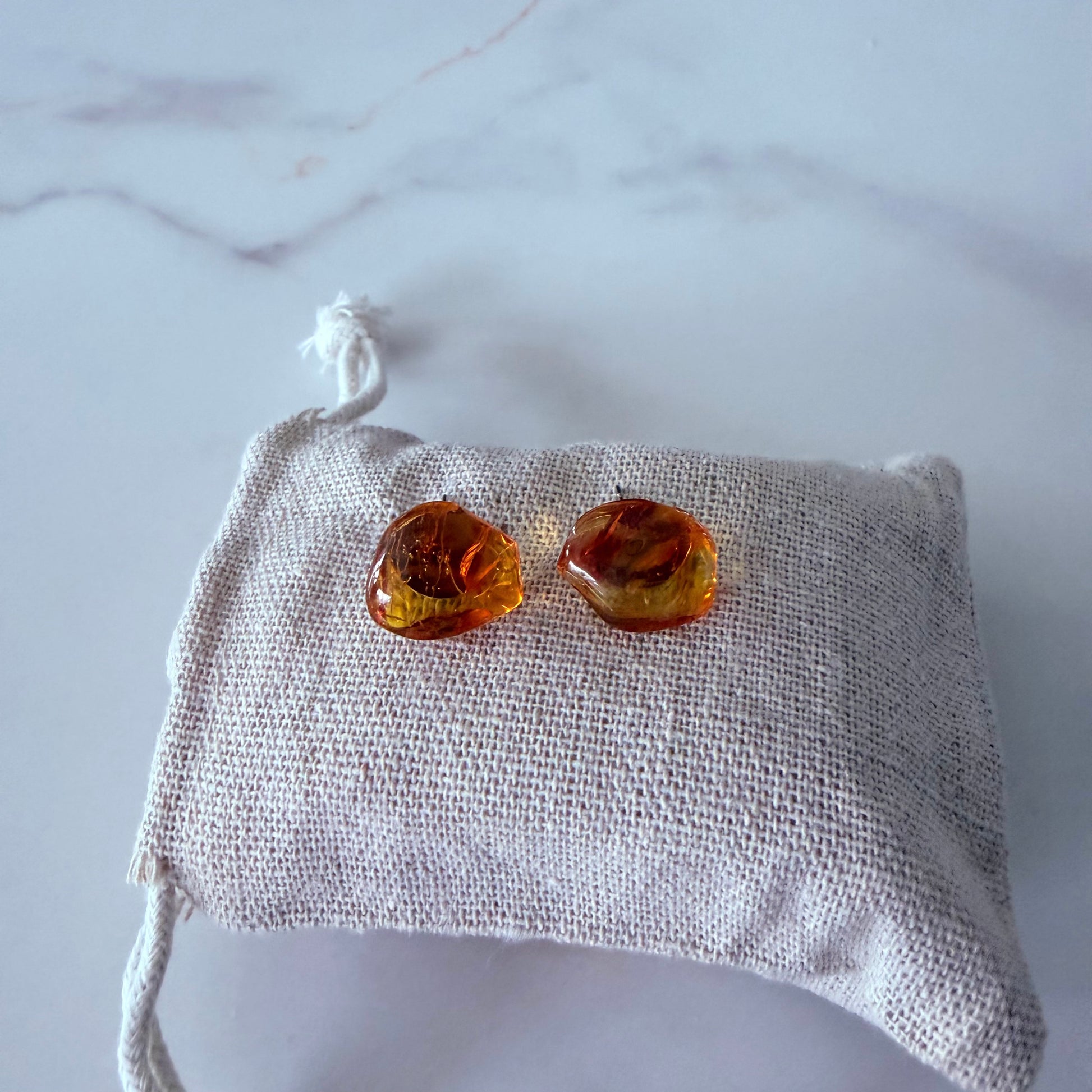 Pair of amber-colored earrings on a textured white pouch against a marble background