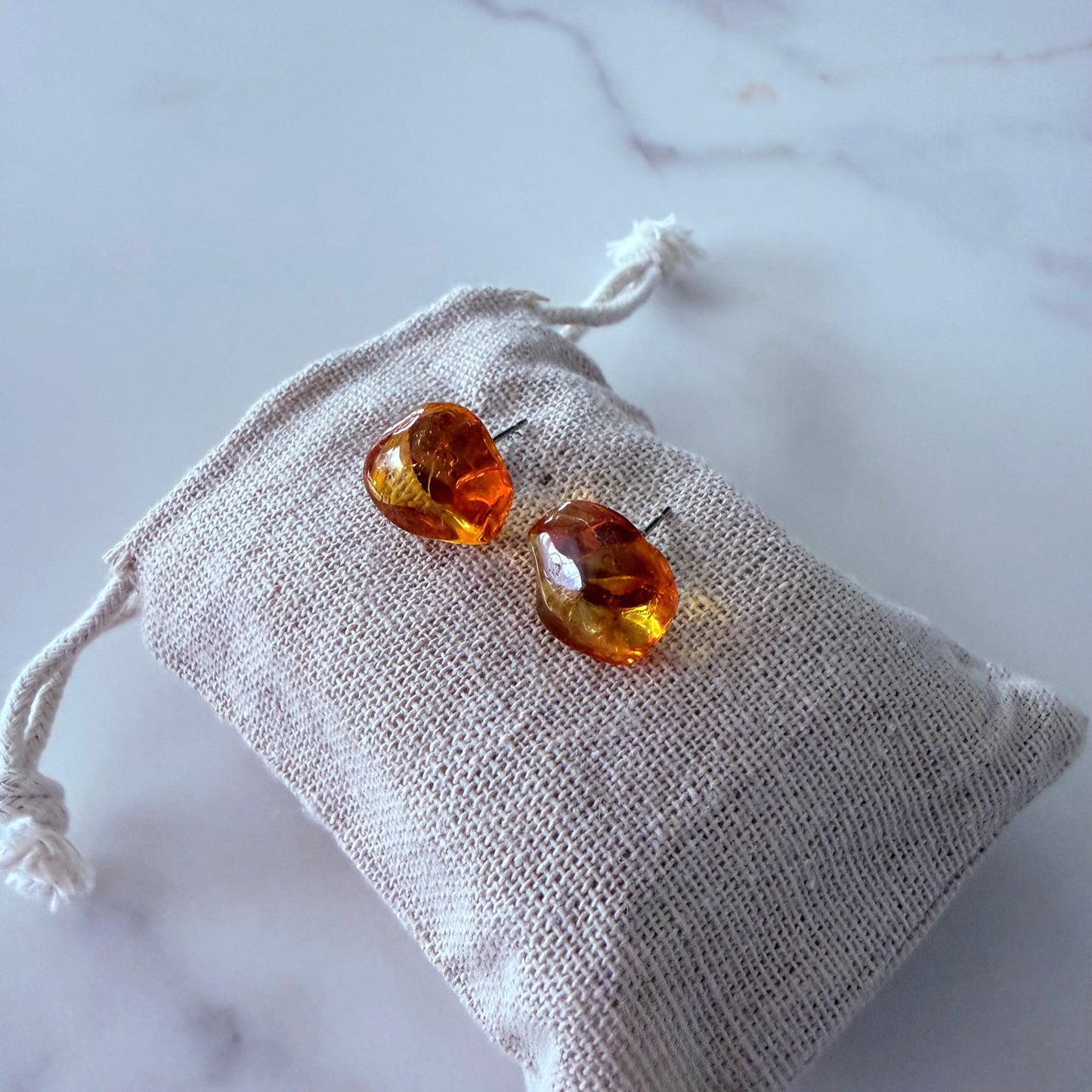 Amber-colored earrings on a white drawstring bag against a marble background