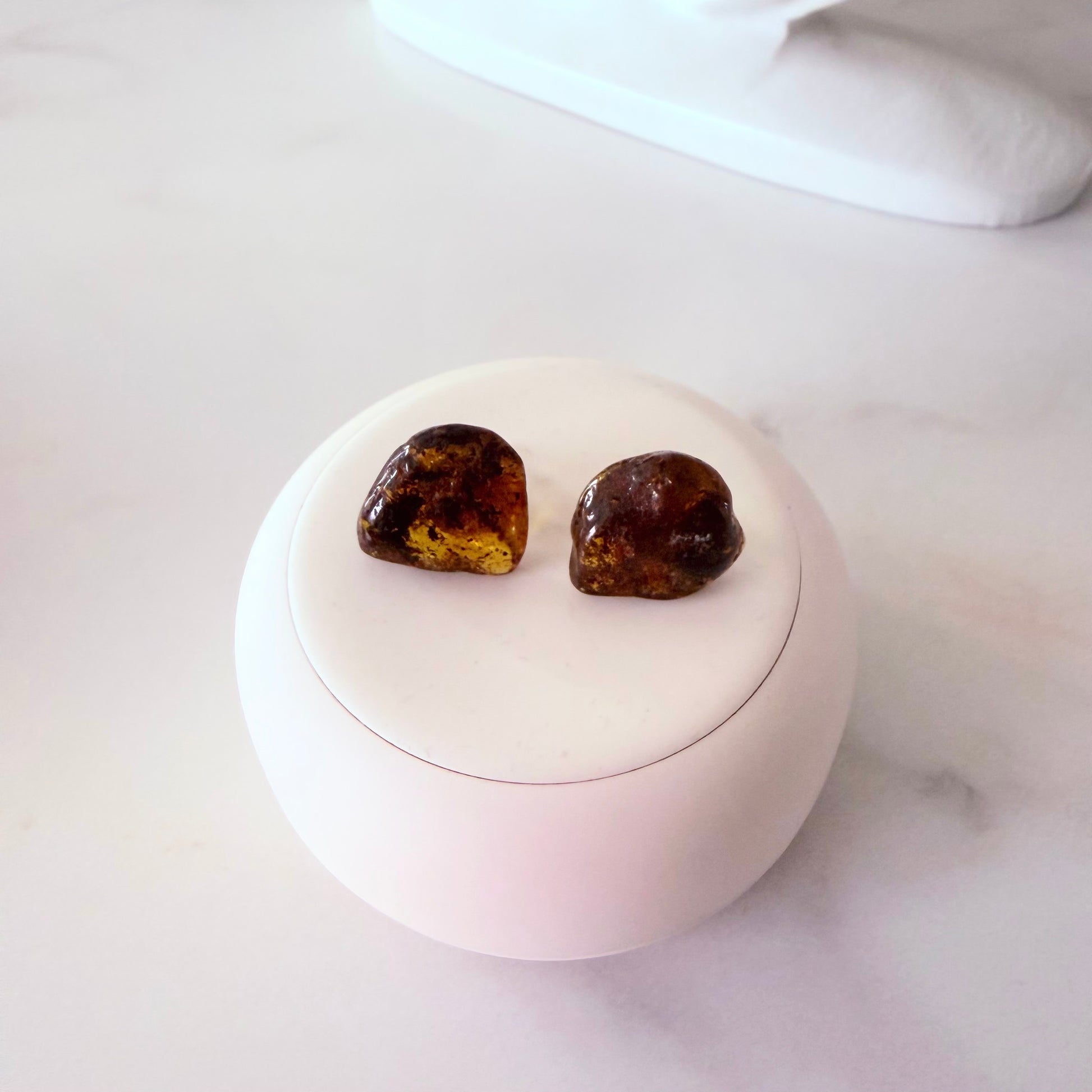 Pair of amber-colored earrings on a white spherical stand with a white background