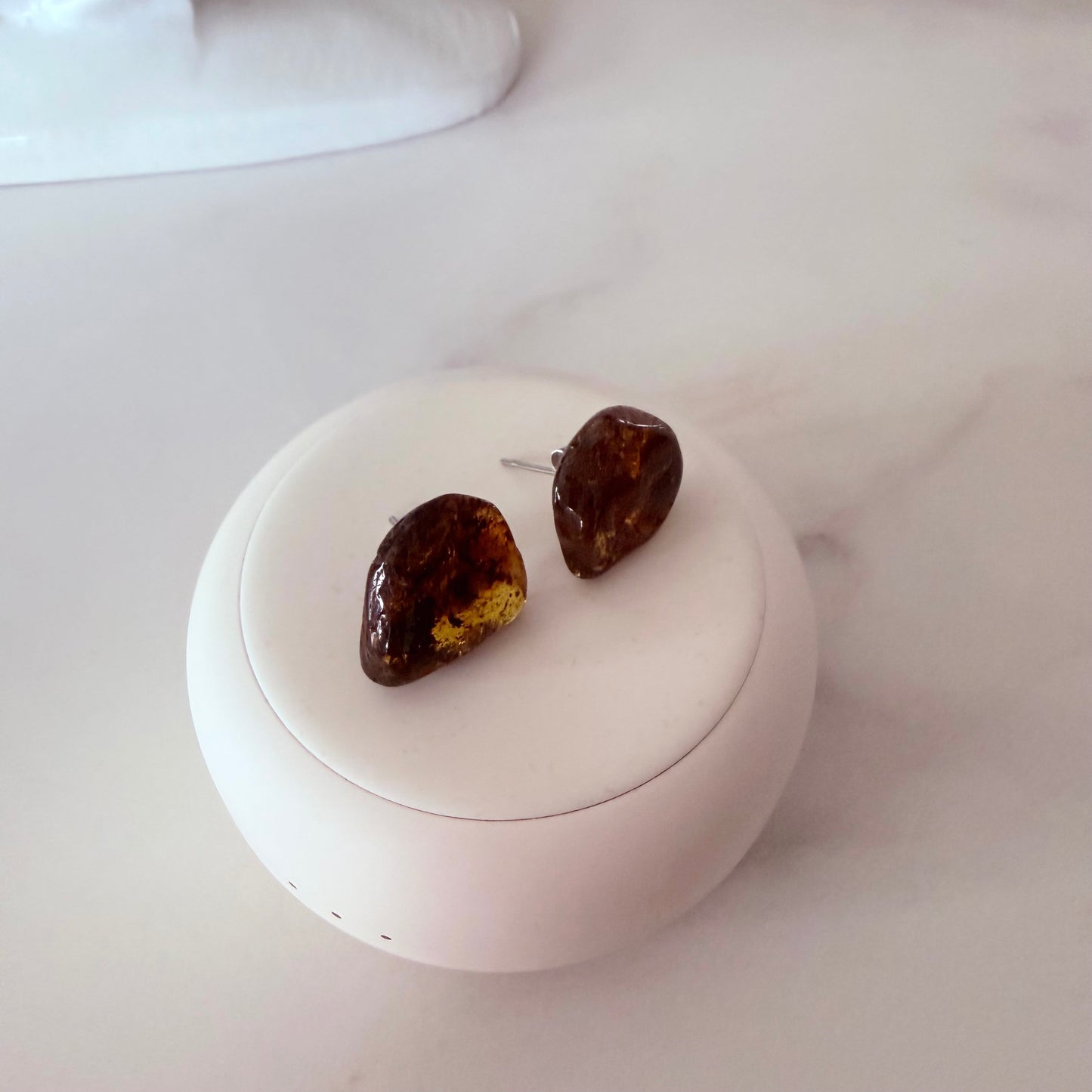 Pair of amber-colored earrings on a white circular stand with a white background