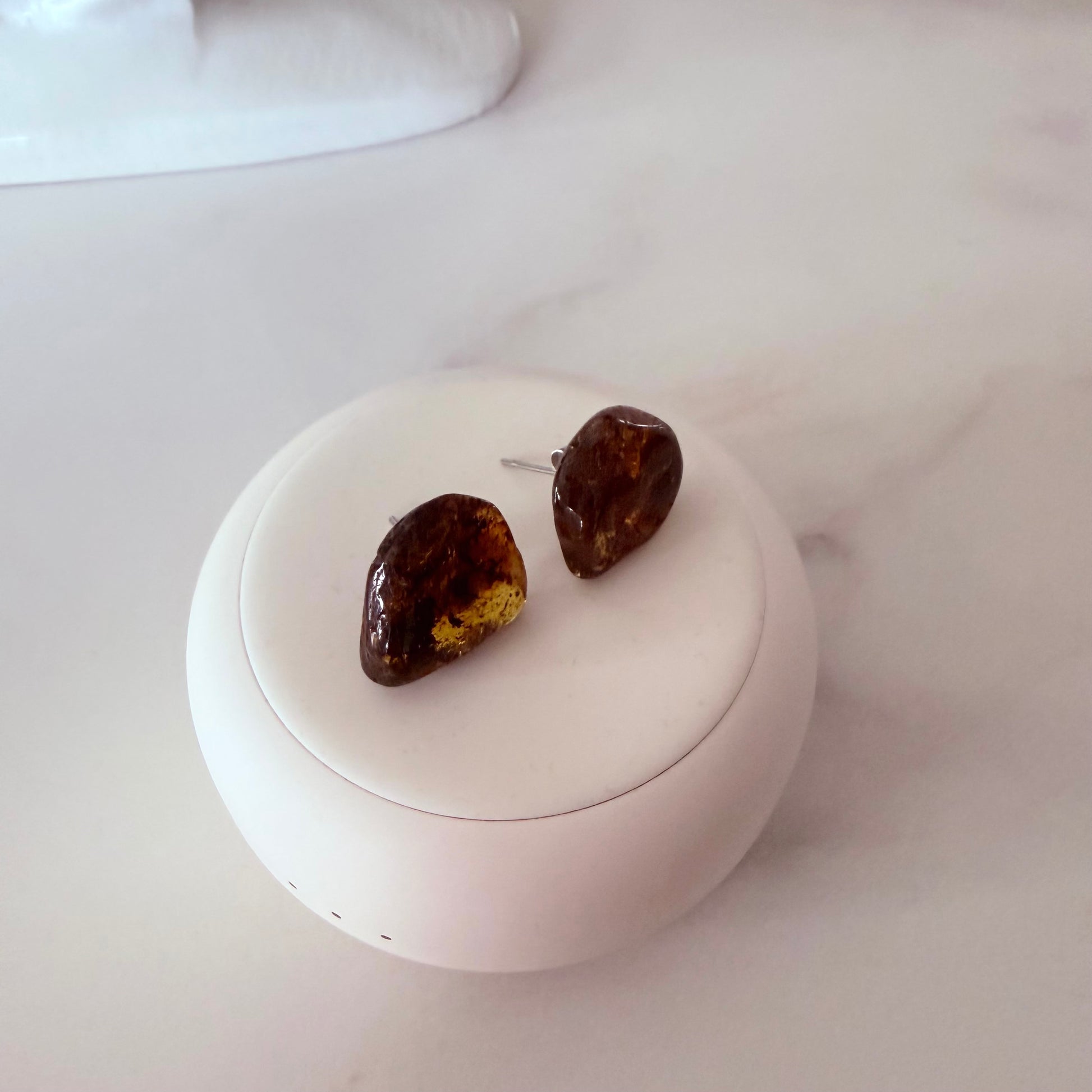Pair of amber-colored earrings on a white circular stand with a white background