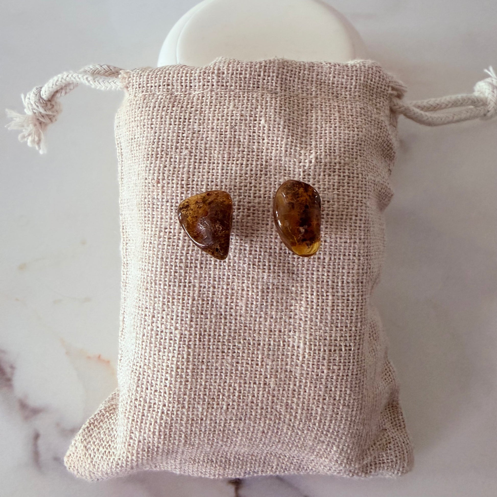 Pair of amber-colored heart-shaped stones in a beige drawstring bag on a marble surface.