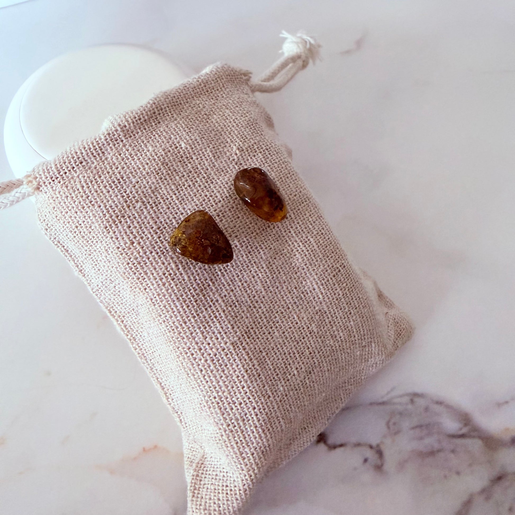 Two amber stones in a beige drawstring bag on a marble surface