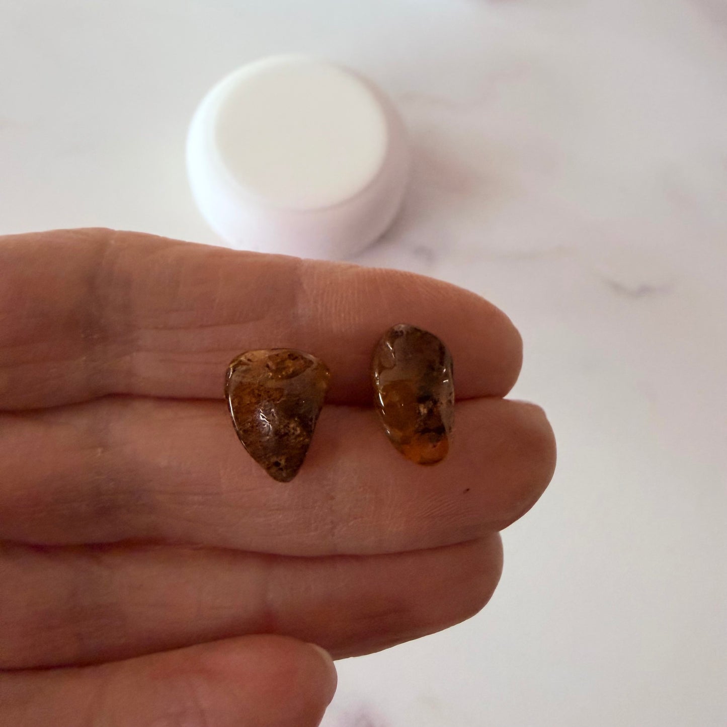 Two amber stones held between fingers with a white container in the background.
