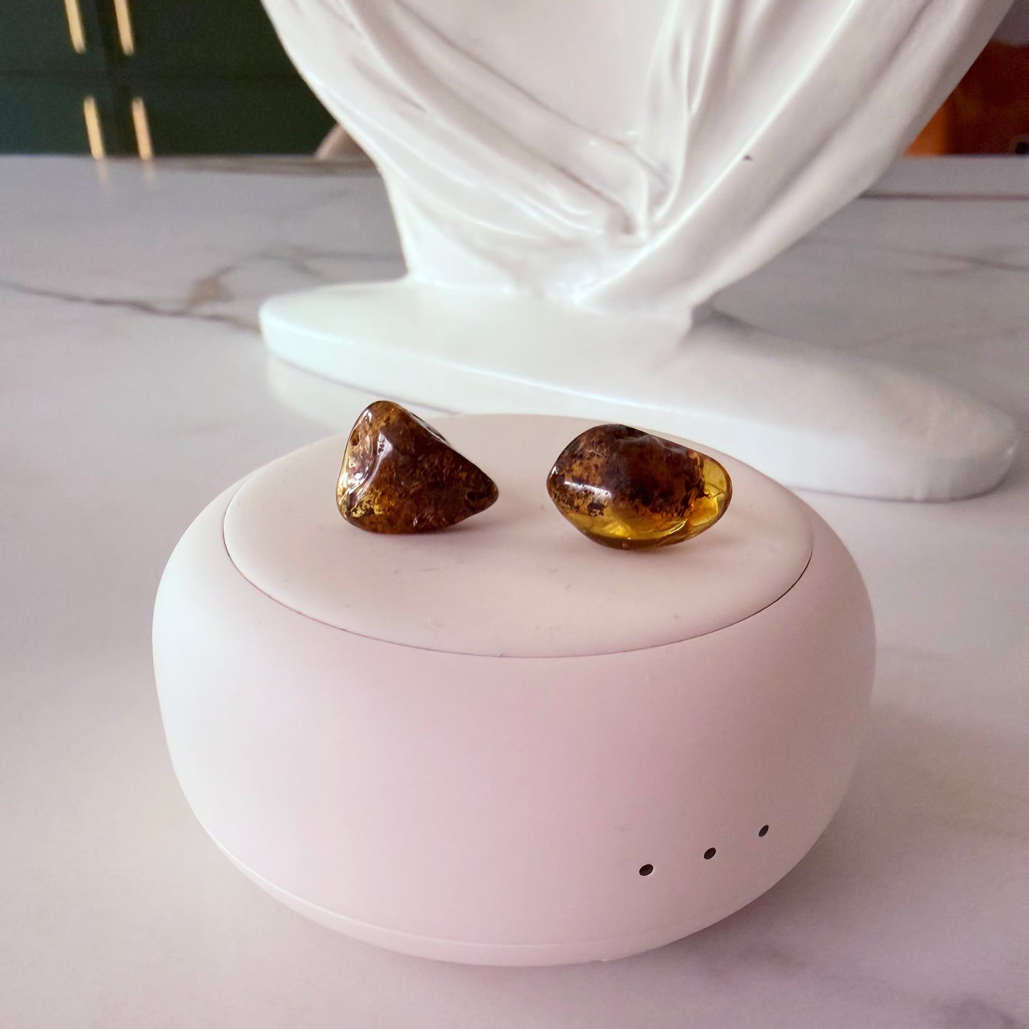 Pair of amber-colored earrings on a white spherical container with a decorative white base.